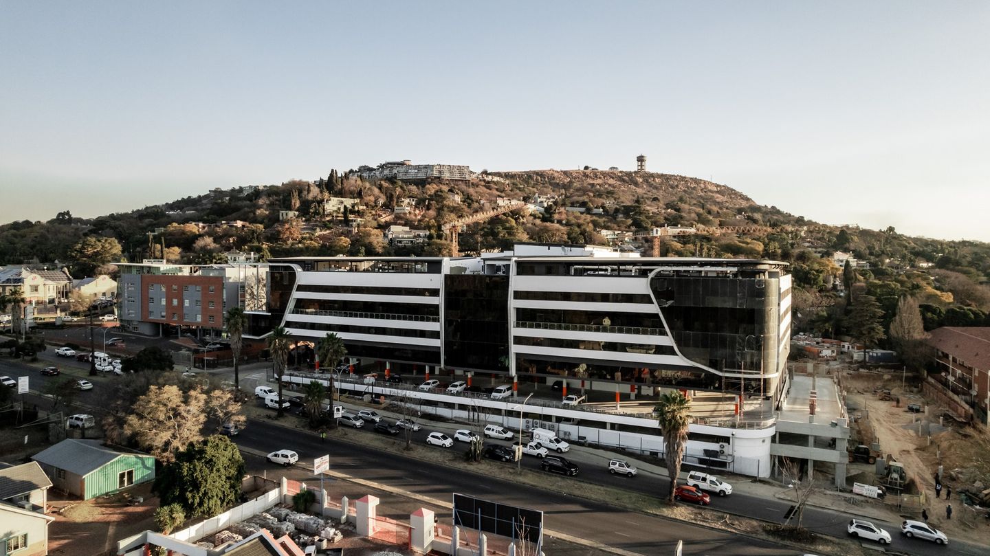 Aerial view of Johannesburg Surgical Hospital, a modern white building with curved bands of glass, at the foot of Northcliff hill.